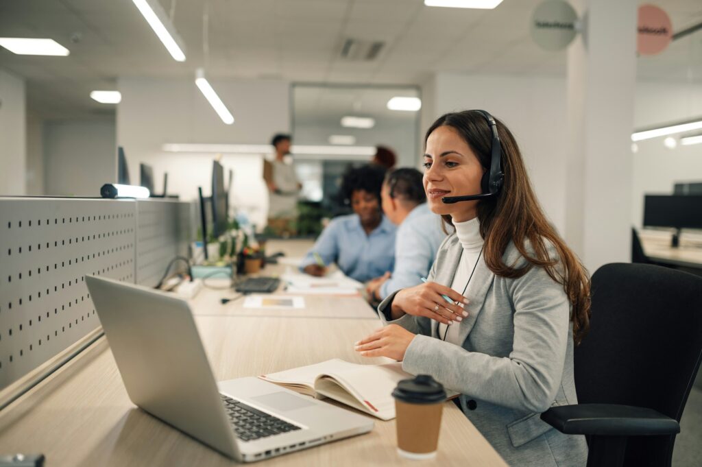 Beautiful woman with headset working on a laptop and talking with clients